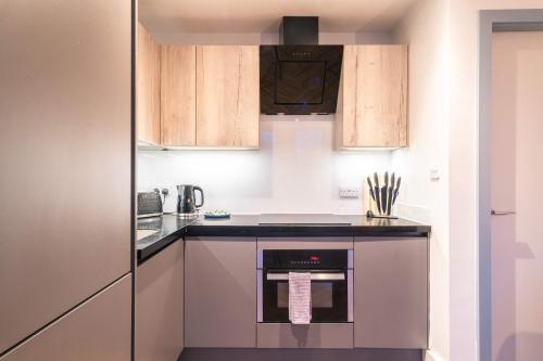 a kitchen with wooden cabinets and a stove top oven at Stunning 2BED Flat in Central Location w Security in Manchester
