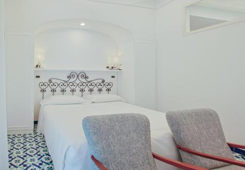 a bedroom with a white bed and two chairs at Hotel Aurora in Amalfi