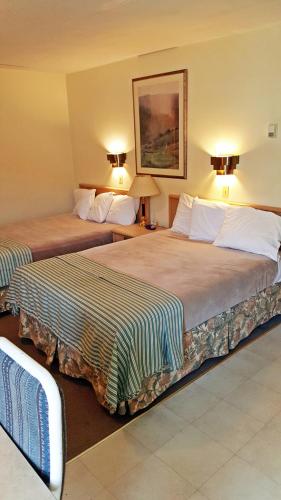 two beds in a hotel room with lamps on the wall at Badlands Motel in Drumheller