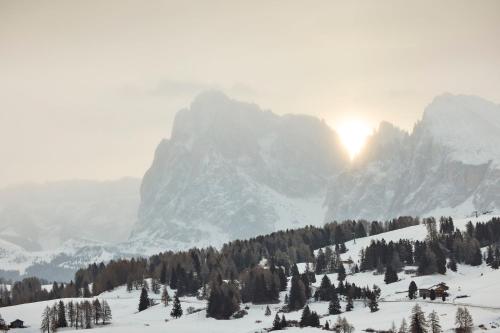 a snow covered mountain with the sun in the background at COMO Alpina Dolomites in Alpe di Siusi