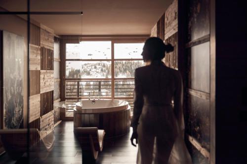 a woman standing in a bathroom looking out a window at COMO Alpina Dolomites in Alpe di Siusi