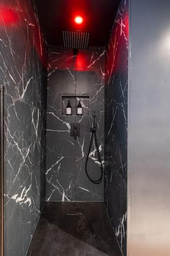 La salle de bains est pourvue d'une douche et de murs en marbre noir. dans l'établissement Le Boudoir Secret - Love Room avec Chambre Secrète, au Luc