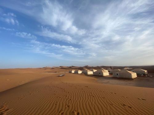 a group of camels in a desert with a sky at Camp Sahara Feeling in El Gouera