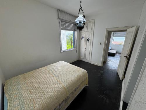 a white bedroom with a bed and a window at Apartamento em frente ao mar in Guarujá