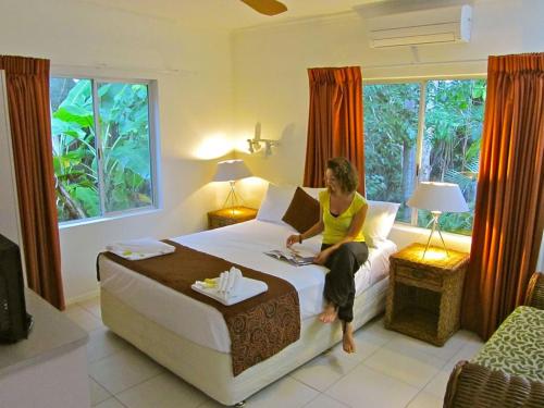 una donna seduta su un letto in una stanza d'albergo di Villa Marine Holiday Apartments Cairns a Yorkeys Knob