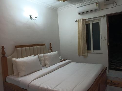 a bedroom with a bed with white pillows and a window at White Guest House in Candolim