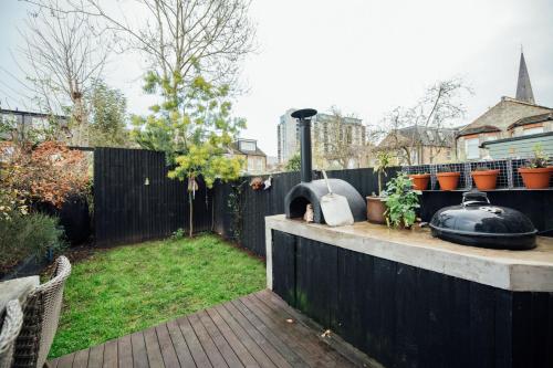 a backyard with a pizza oven and plants on a fence at Stylish 2 Bedroom Flat with a Private Sauna in Finchley