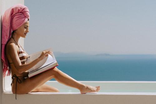 a woman sitting on a ledge reading a book at Gazelle Living in Imerovigli