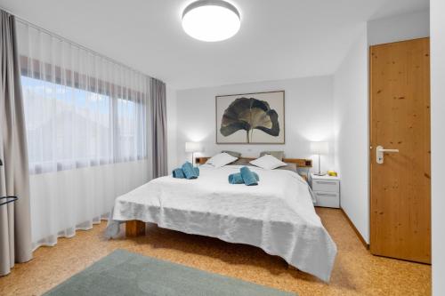 a white bedroom with a large bed and a window at Gemütliche 2.5 Zimmer Wohnung mit privater Sauna in Seewis im Prättigau
