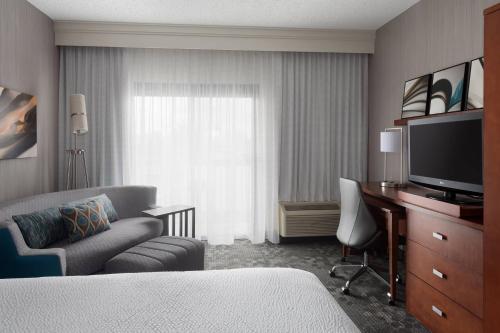 a hotel room with a bed and a desk with a television at Courtyard Syracuse Carrier Circle in East Syracuse