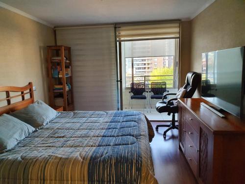 a bedroom with a bed and a desk and a television at Departamento con AC Ñuñoa in Santiago