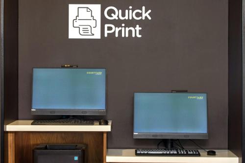 two computer monitors sitting on a desk with a keyboard at Courtyard by Marriott Phoenix North in Phoenix