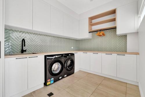 a washing machine in a kitchen with white cabinets at Seven Mile View Gerroa in Gerroa
