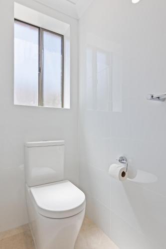 a white bathroom with a toilet and a window at Elegant 3-Bed Home Steps from Sunny Glenelg Beach in Glenelg