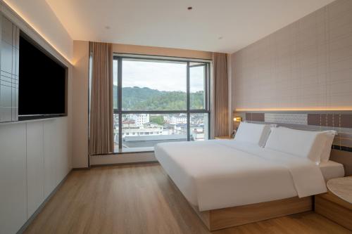 a bedroom with a large white bed and a large window at Zhangjiajie Homeinn Plus Hotel in Zhangjiajie