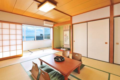 a room with a table, chairs, and a window at Onsen Hostel Hinoemi in Atami