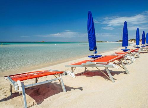 a row of lounge chairs and blue umbrellas on a beach at Tramontana Villa 30 Meters From the Beach no4687 in Torre Specchia Ruggeri