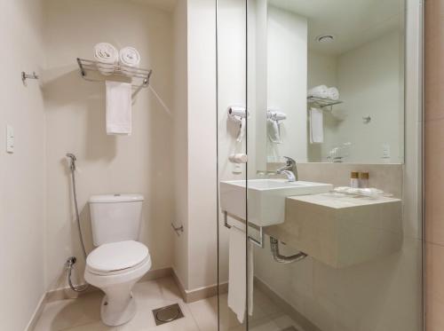 a white bathroom with a toilet and a sink at Tulip Inn Sete Lagoas in Sete Lagoas