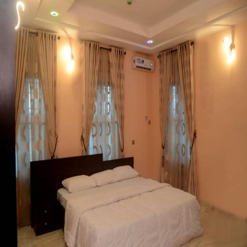 a bedroom with a bed with white sheets and curtains at Mexiloyd Suites Queen Apartment in Port Harcourt
