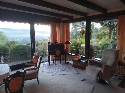a living room with chairs and a piano and large windows at Ferienhaus am Breitenbach-Stausee in Hilchenbach