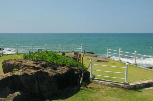 a large rock next to the ocean with a fence at Amara White Villa in Ahungalla