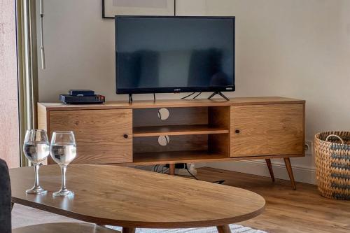 une télévision sur un meuble de divertissement en bois avec deux verres à vin dans l'établissement Carla - vue mer clim wifi parking - by TGB, à Ajaccio