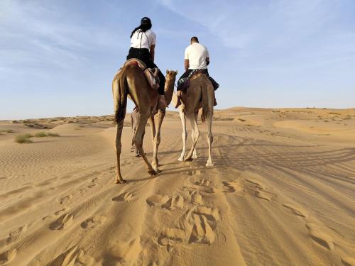 zwei Menschen reiten auf Pferden in der Wüste in der Unterkunft The One - Sunset private Tent camp in Badīyah