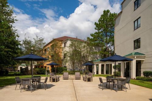 コビントンにあるCourtyard by Marriott Covington / Mandevilleのテーブルと椅子とパラソルのあるパティオ