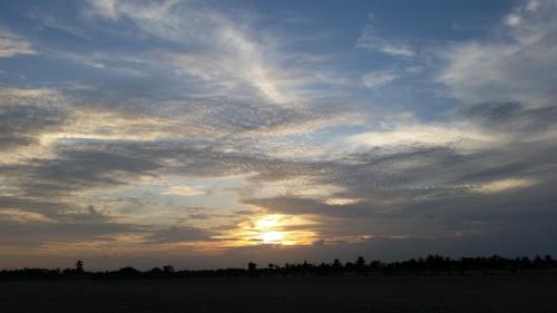a cloudy sky with the sun setting in a field at A&Y Wild Camp Ghana in Keta