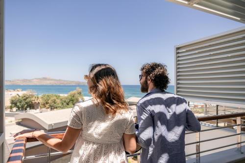 a man and a woman standing on a balcony looking out at the ocean at Cretan Dream Resort & Spa in Stalos