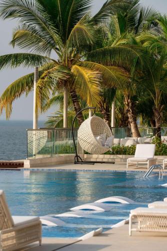 a swimming pool with chairs and palm trees next to the ocean at Radisson Blu Hotel, Conakry in Conakry