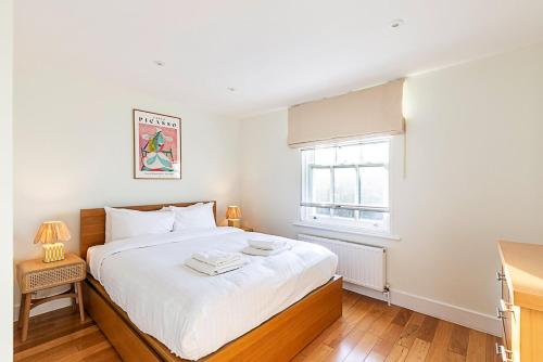 a bedroom with a large white bed with a window at Stylish Chelsea Flat with Luxe Comfort & Charm in London