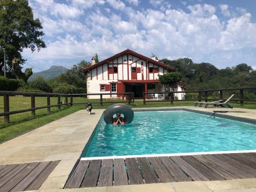 une personne dans une piscine avec une maison en arrière-plan dans l'établissement Maison de caractère au calme et vues magnifiques, à Sare