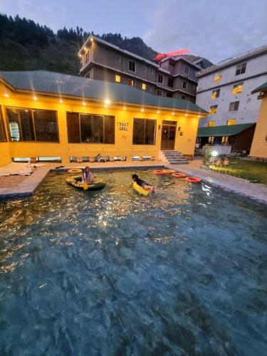 two people in kayaks in the water in front of a building at Trout Lodges Naran in Naran