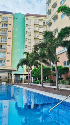 a swimming pool with palm trees in front of a building at Tessa's Place Staycation 10FI in Jalang