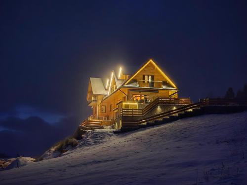 a large wooden house in the snow at night at LK Mountain Residence segmenty z prywatnym jacuzzi i widokami na góry i jezioro in Falsztyn