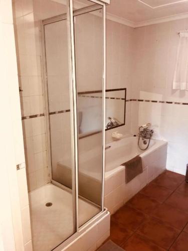 a glass shower in a bathroom with a tub at Hlalanathi Drakensberg Resort in Bergville