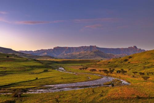 a river in a field with mountains in the background at Hlalanathi Drakensberg Resort in Bergville