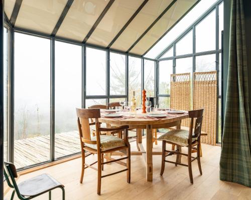 une salle à manger avec une table, des chaises et des fenêtres dans l'établissement Le Douillet - Superbe maison au calme en campagne, à Laferté-sur-Amance