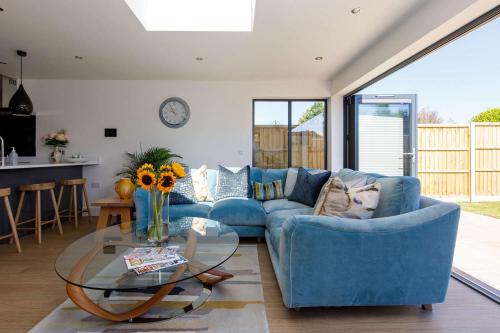 a living room with a blue couch and a glass table at Luxury designer coastal home for 10 with hot tub in West Wittering
