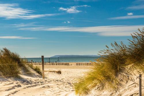 a sandy beach with a fence and the ocean at Luxury designer coastal home for 10 with hot tub in West Wittering