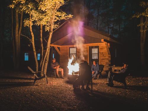 a group of people sitting around a fire in front of a cabin at Mini-Chalet - Abenaki Aventure in Pierreville
