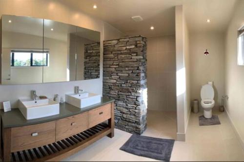 baño con 2 lavabos y pared de piedra en Bluewater Sanctuary Spectacular Coastal Views, en Tutukaka