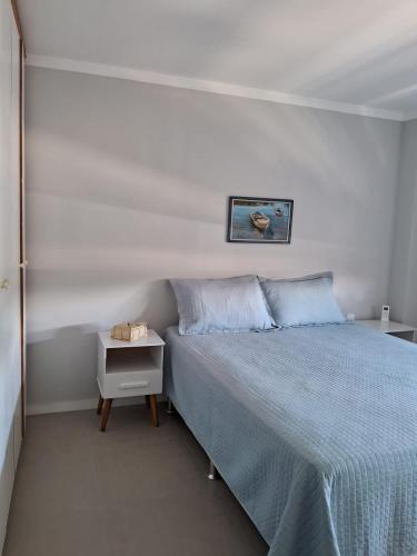 a white bedroom with a blue bed and a night stand at Apartamento novo entre a praia dos Ingleses e Santinho in Florianópolis