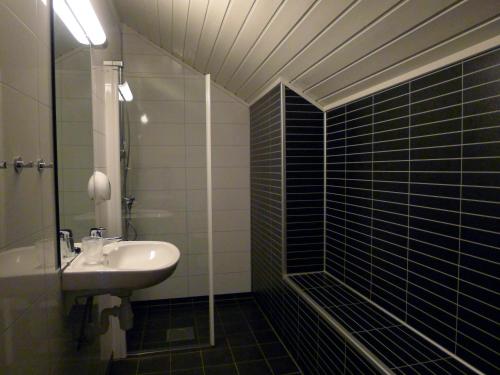 baño de azulejos negros con lavabo y ducha en Jostedal Hotel en Jostedal