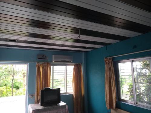 a room with blue walls and a tv and windows at Gayatri Holiday Home in Murud