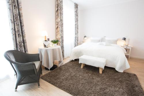 a white bedroom with a bed and a chair at Hotel Strand26 an der Ostsee in Ostseebad Nienhagen