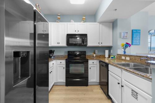 Una cocina con gabinetes blancos y un refrigerador negro. en Stunning Resort 11th Fl Pool & Gulf View King Suite Across From Beach, en Destin