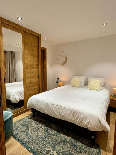 une chambre avec un grand lit blanc et un miroir dans l'établissement Woodpecker Appartement au coeur du village, aux Houches
