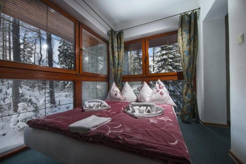 a bedroom with a red bed with pillows and windows at Penzión Pleso in Vysoke Tatry - Strbske Pleso